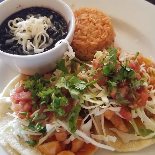 Two Favela's Mexican Grill tacos with rice and a bowl of black beans with cheese.