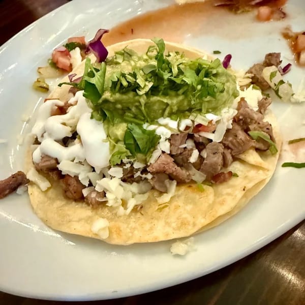 A Favela's Mexican Grill taco with meat, guacamole, sour cream, and cheese on a white plate.