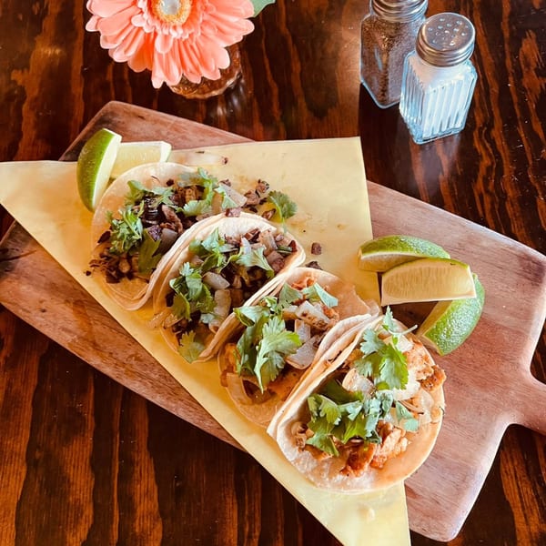 Four Favela's Mexican Grill tacos with meat, onions, and cilantro, served with lime wedges.