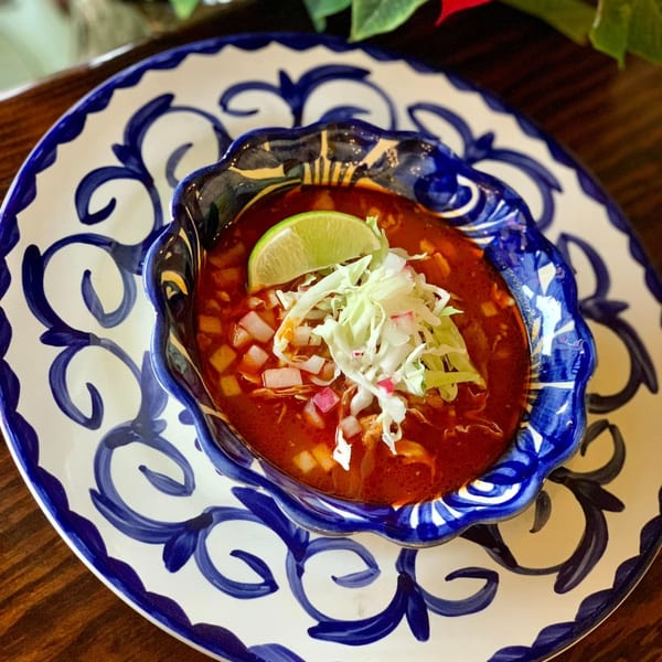 A bowl of Favela's Mexican Grill's red pozole, garnished with shredded cabbage, diced onions, and a lime wedge.