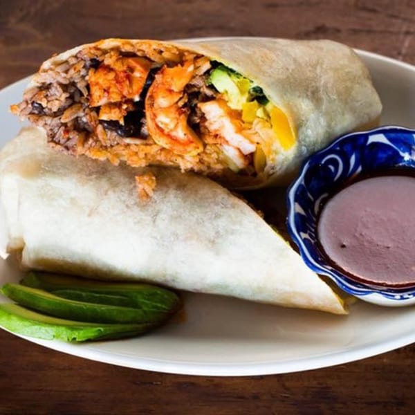 A large, cut Favela's Mexican Grill burrito with rice, shrimp, and avocado, served with sauce.
