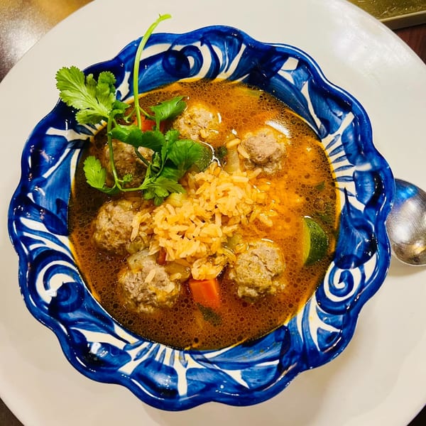 Favela's Mexican Grill's albondigas soup with meatballs, rice, and cilantro in a blue and white bowl.
