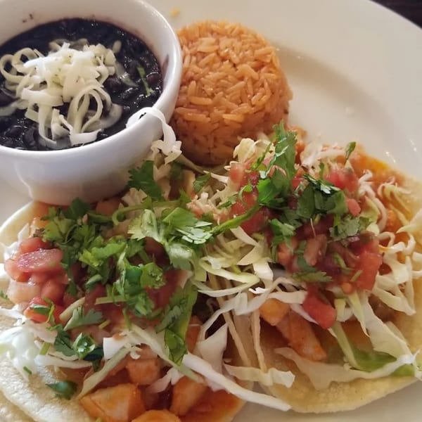 Two Favela's Mexican Grill tacos with rice and a bowl of black beans with onions.