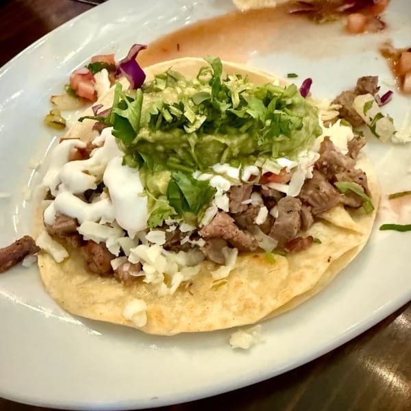 A Favela's Mexican Grill taco with steak, guacamole, sour cream, and shredded lettuce.