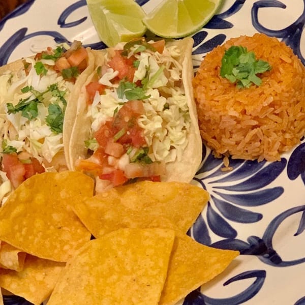 Two tacos with rice, tortilla chips, and lime wedges on a blue and white patterned plate.