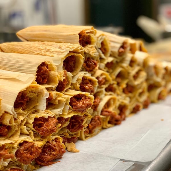 A large pile of Favela's Mexican Grill tamales with red filling, wrapped in corn husks.
