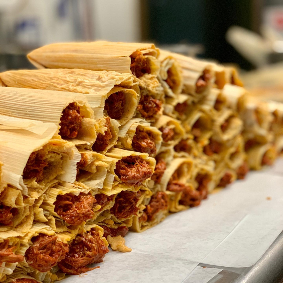 A large pile of Favela's Mexican Grill tamales with red filling, wrapped in corn husks.