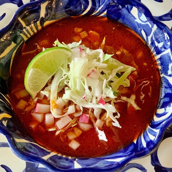 Pozole Rojo, a traditional Mexican soup, garnished with cabbage, radishes, and a lime wedge.