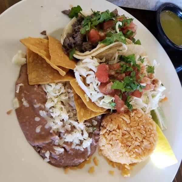 Favela's Mexican Grill plate with two tacos, refried beans, rice, tortilla chips, and a lime wedge.