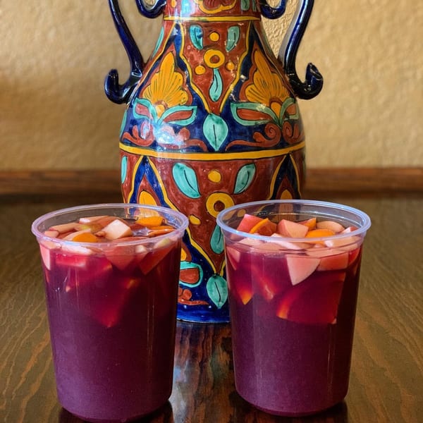 Two cups of sangria with fruit next to a colorful, ornate Mexican pitcher.