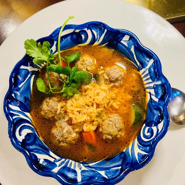 Favela's Mexican Grill's albondigas soup with meatballs, rice, and cilantro in a decorative blue bowl.
