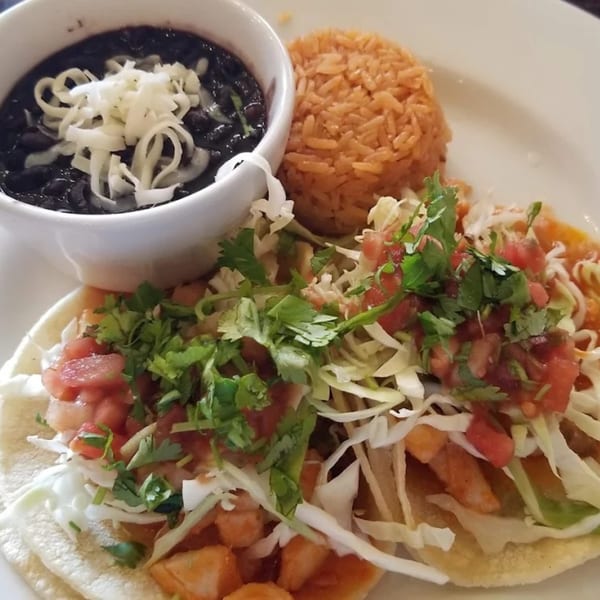 Two Favela's Mexican Grill tacos with rice and a bowl of black beans topped with cheese.