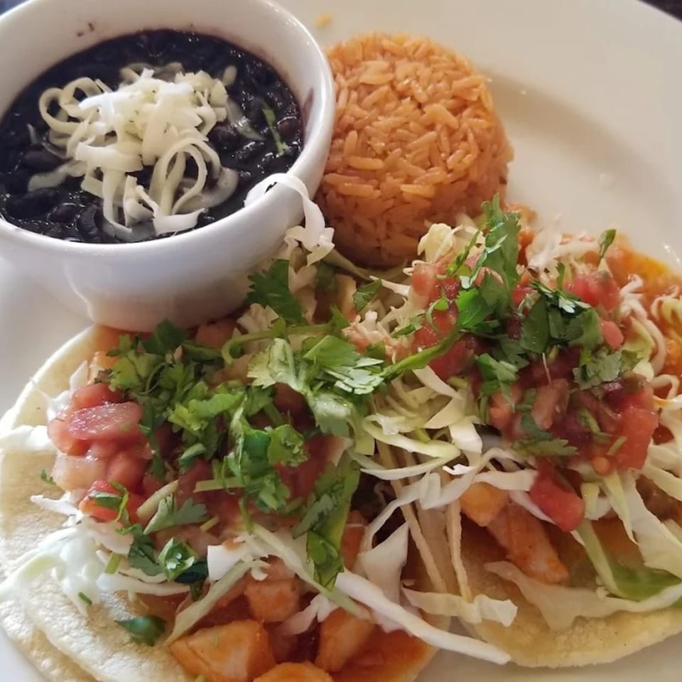 Two Favela's Mexican Grill tacos with rice and a bowl of black beans topped with cheese.